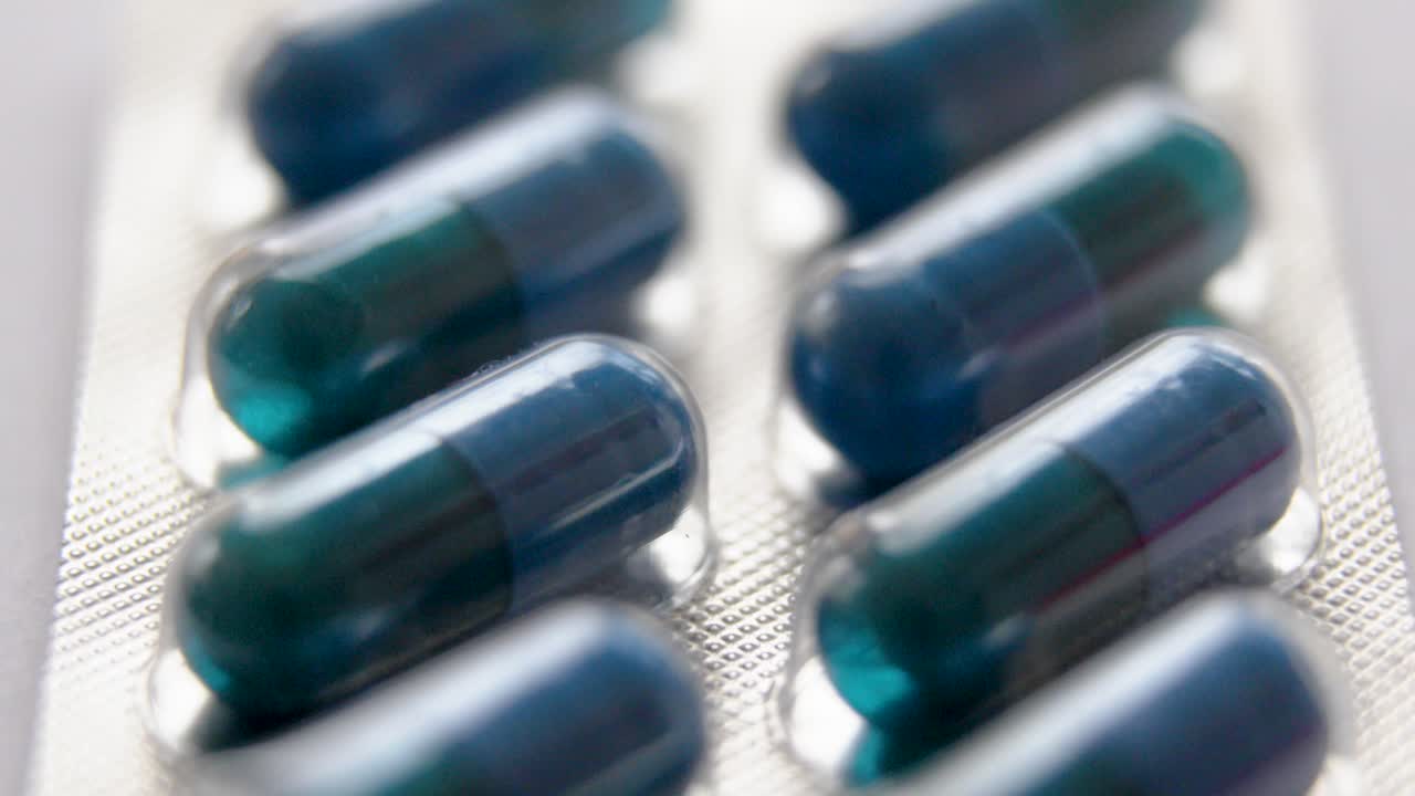 a very close-up vertical shot from top to bottom of an aluminium and plastic plate filled with hermetically sealed blue and dark green capsules