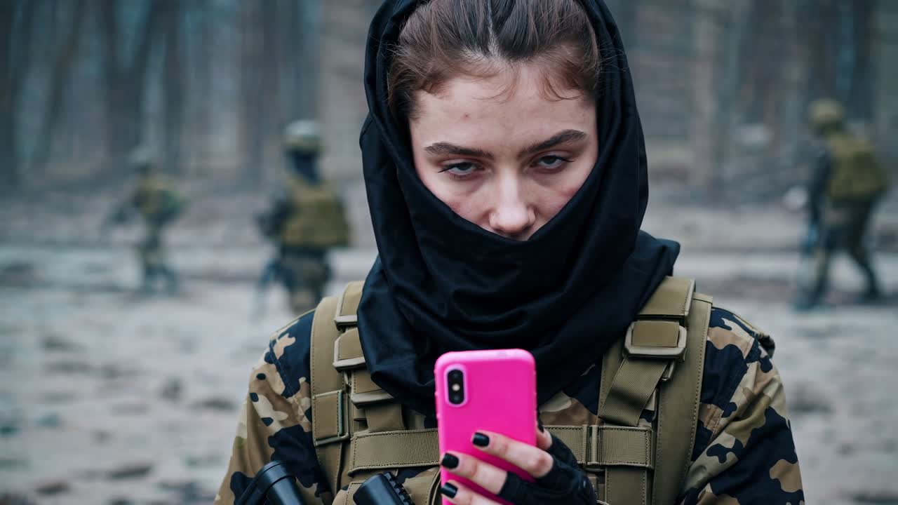 Female soldier. Equipped with tactical gear and a partially obscured face. Using a smartphone amidst blurred fellow soldiers on a desolate battlefield. Emphasizing technology's role in modern warfare
