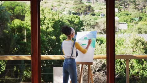 mixed race woman painting on canvas in the balcony at home