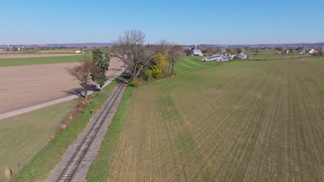 an aerial view of a single rail road track going thru country farmlands on a sunny fall day