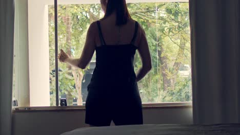 정원이 내려다보이는 침실 창문을 여는 반바지와 티셔츠를 입은 여성의 뒷모습