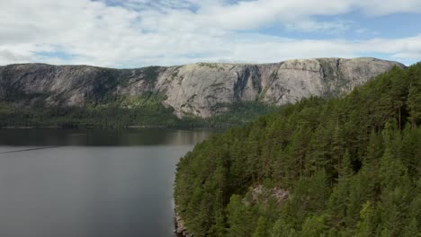 aerial past a forest on the nisser lake and the langfjell mountain range in the background, treungen, telemark, norway