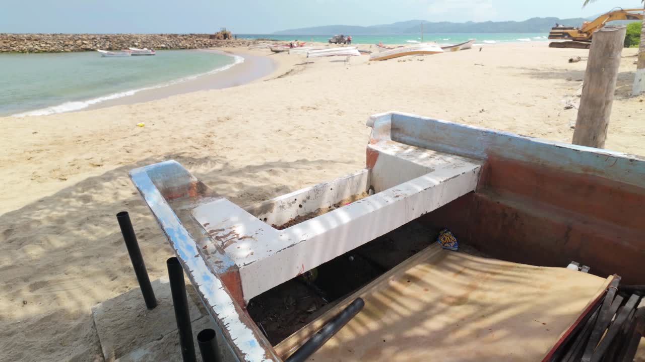 A stranded boat rests on a sandy beach beneath palm trees. Sunlight filters through the leaves, casting gentle shadows on the sand. The tranquil atmosphere evokes a sense of solitude and peace.