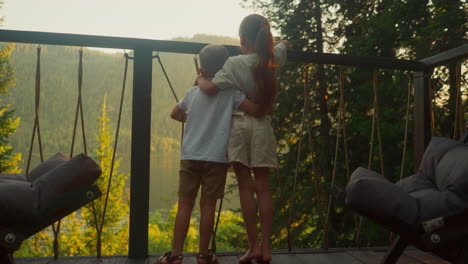 hermano y hermana disfrutan de un viaje de glamping admirando la belleza escénica del bosque sumergiéndose en el entorno natural. niño y niña se abrazan en el balcón viendo el entorno en cámara lenta