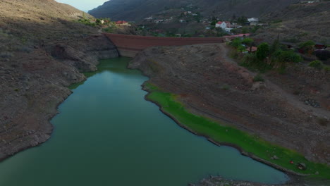 Presa-De-Ayagaures,-Gran-Canaria:-Fantástica-Vista-Aérea-Recorriendo-El-Muro-De-Contención-De-La-Presa-En-Un-Día-Soleado-Y-En-Un-Entorno-Natural-Privilegiado