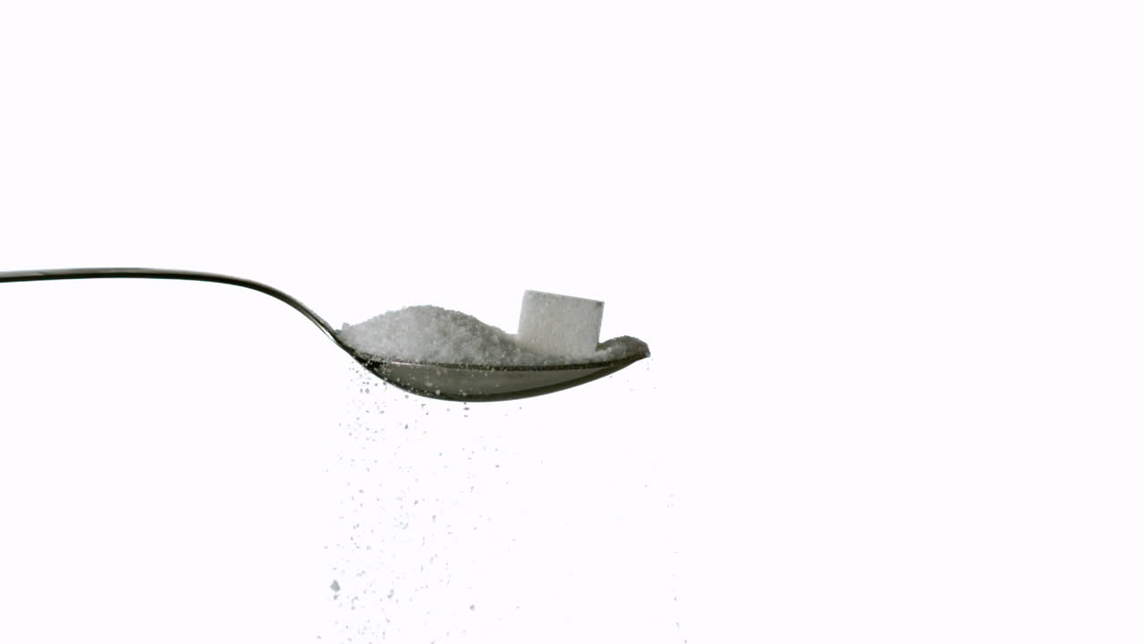 Sugar spilling off spoon with sugar and sugar cube