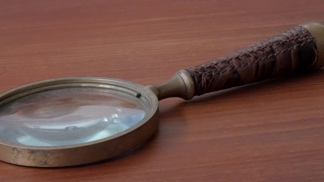 Smooth pan right showing an antique magnifying glass with metal frame on wooden table