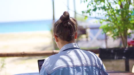 mujer trabajando en una computadora portátil vista desde atrás en la playa con vista al mar