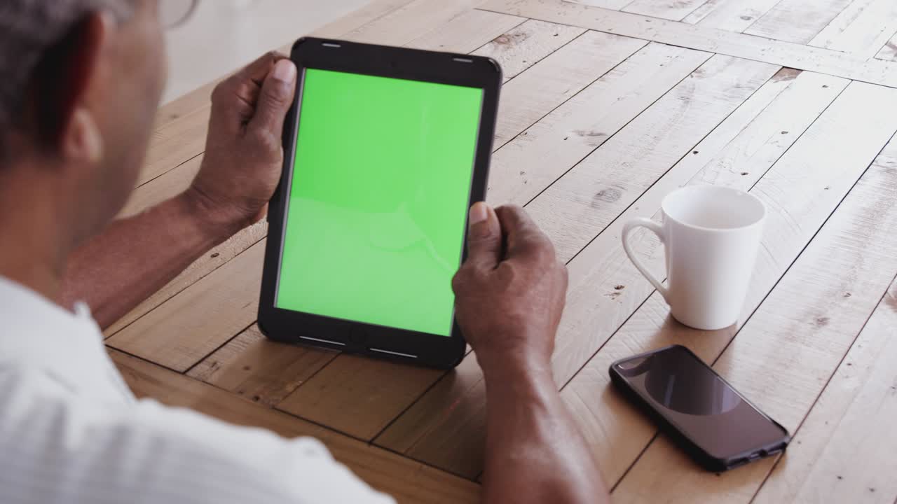 vista por encima del hombro de un hombre negro mayor en una mesa de madera usando una computadora tablet, de cerca