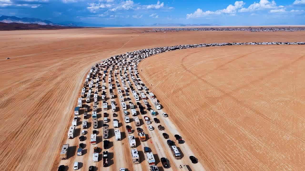 Long vehicle queue on desert entry road. A massive curved line of cars and RVs moves slowly across the open desert plain