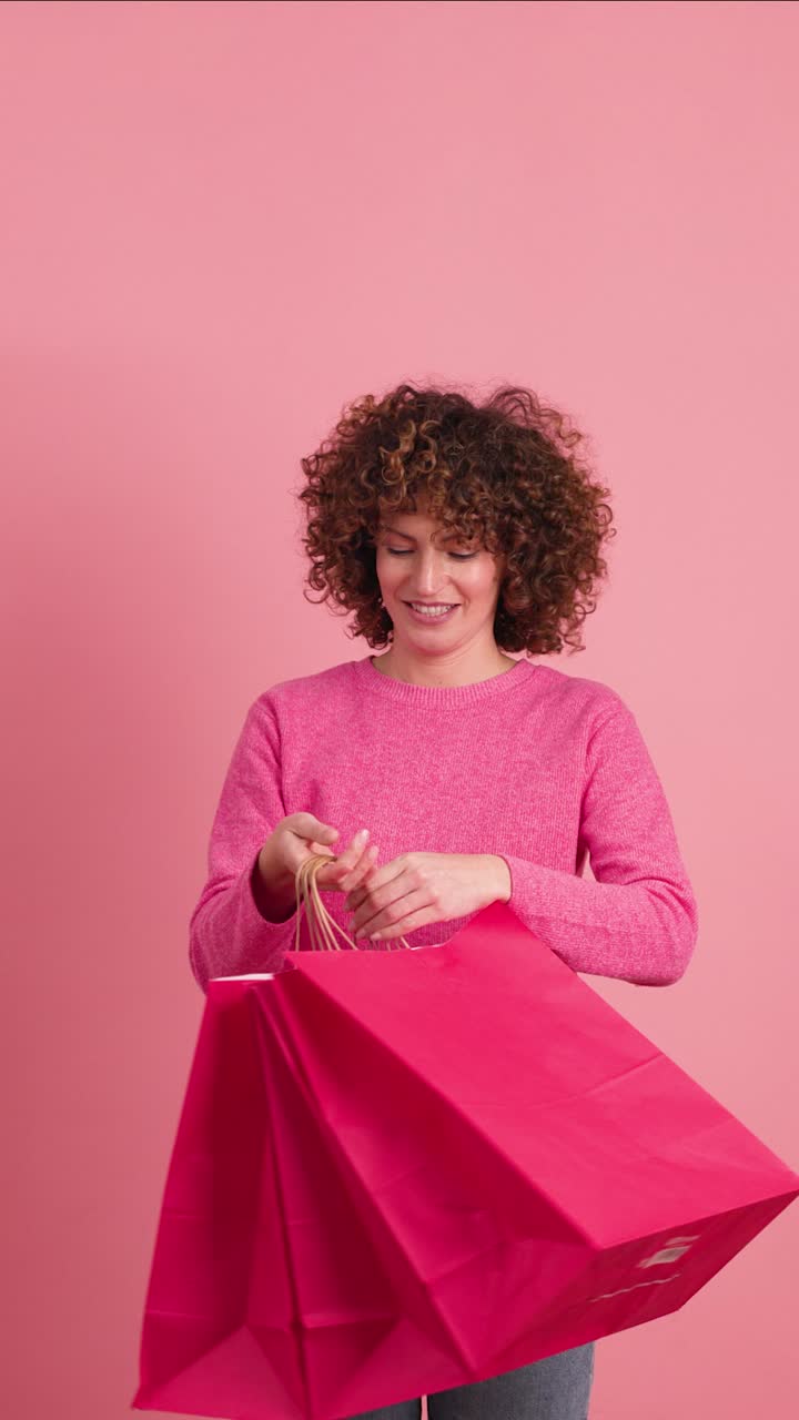 Happy woman with shopping paper bags in pink studio. Vertical footage