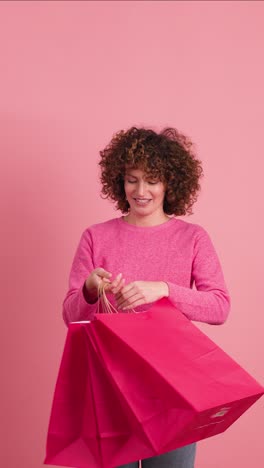 happy woman with shopping paper bags in pink studio. vertical footage