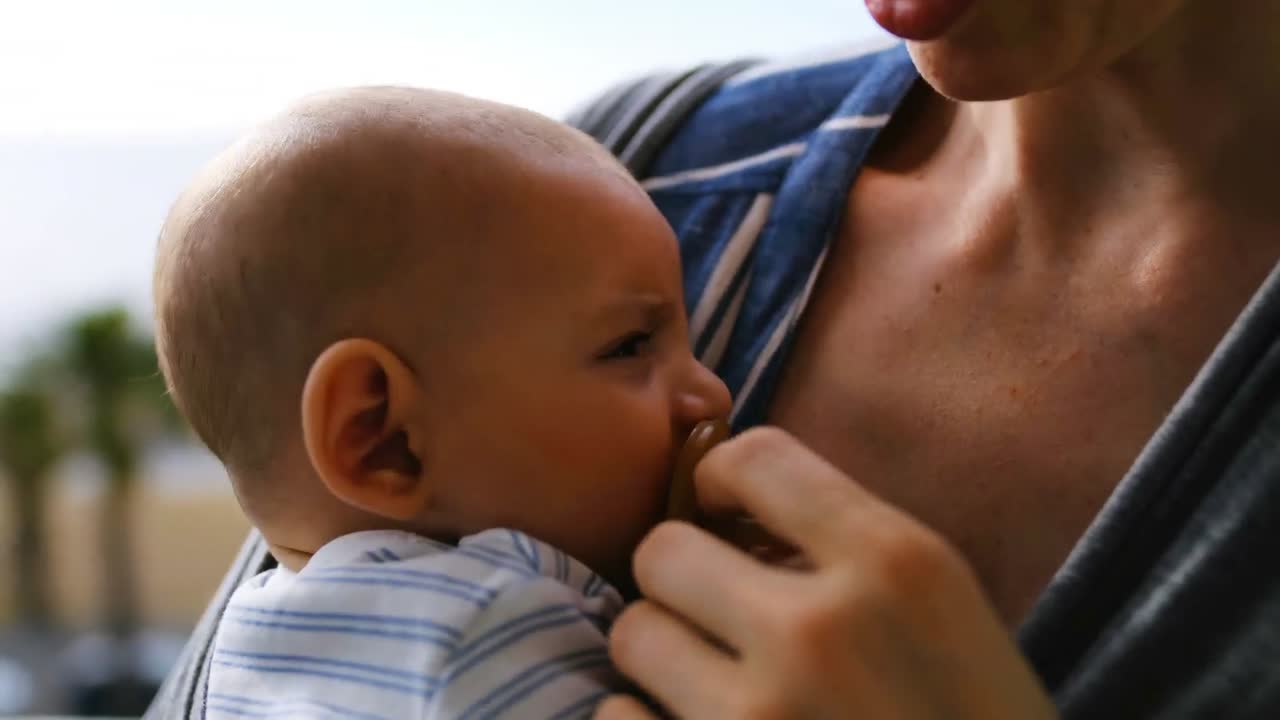 madre joven consolando a un bebé llorando en un sling en casa 4k
