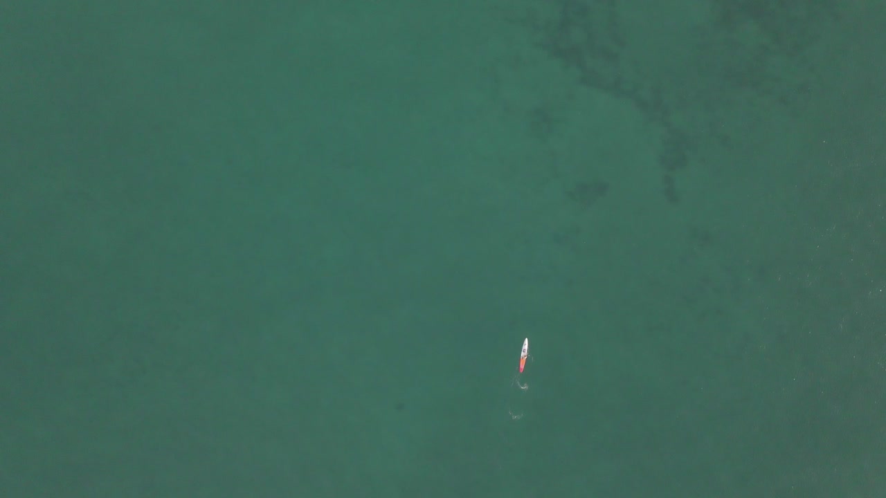 antena vertical mira hacia abajo sobre un paddleboarder solitario en un mar verde poco profundo
