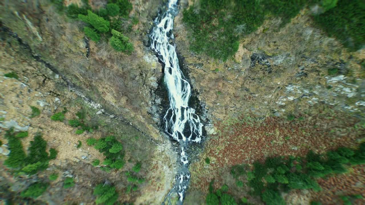 Drone rises vertically above Bâlea Waterfall in Romania, camera pointing straight down, waterfall in the center, capturing dramatic perspective and mountain scenery
