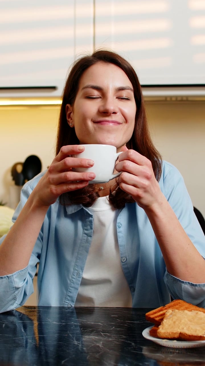 Mujer joven disfrutando de un café caliente en una cocina moderna, sintiendo una agradable satisfacción durante el desayuno matutino.