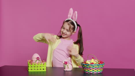 smiling confident toddler placing bunny ears on her head and waving