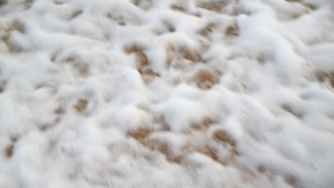 Schäumende-Welle-Spült-In-Zeitlupe,-Nahaufnahme,-über-Orangefarbenen-Sand