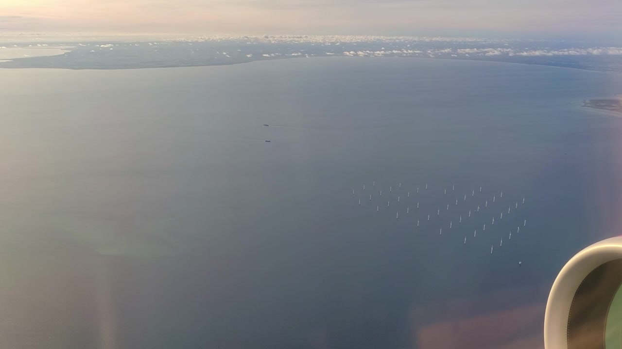 デンマークの洋上風力発電所。風車、海、船が見える。飛行機の窓から、エンジンと窓の反射越しに撮影。
