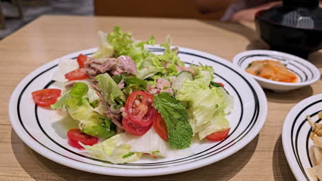 a serving of tuna salad served in a platter with side dishes like kimchi and miso soup and eaten by a customer with a pair of chopsticks inside a restaurant in bangkok, thailand