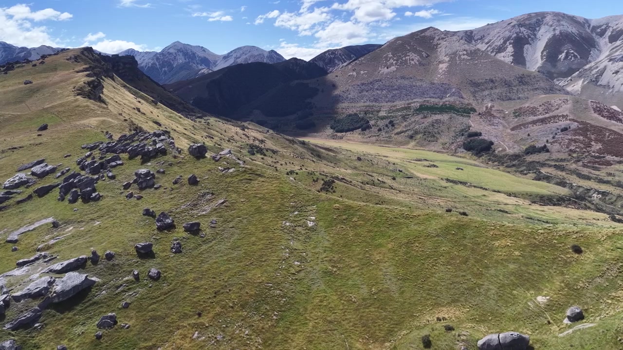 Una vista aerea sorvola una cresta montuosa erbosa con rocce sparse sotto un cielo blu.