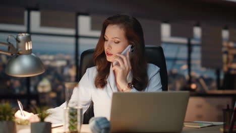 business woman speaking smartphone at night workplace. calling lady making notes