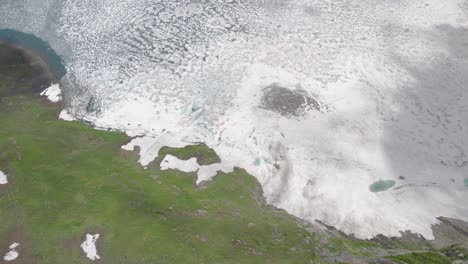 lago cubierto de nieve con manchas verdes y agua azul en la vista de pájaro de la montaña