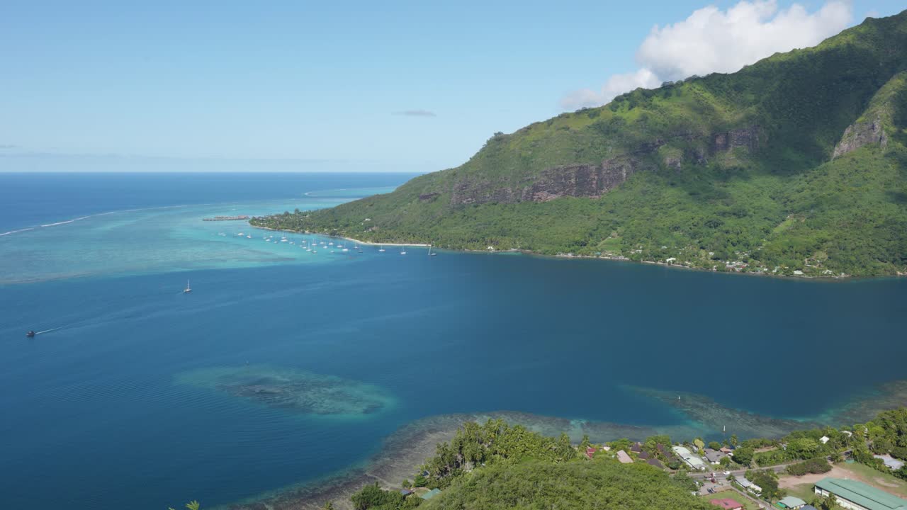 View of mountains and the ocean on a sunny day in a small green tropical pacific island from Magic Mountain, Moorea, French Polynesia.