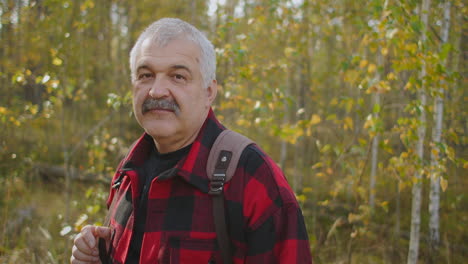 retrato de un turista de cabello gris con bigote en el bosque en un día de otoño el hombre está sonriendo a la cámara ecoturismo