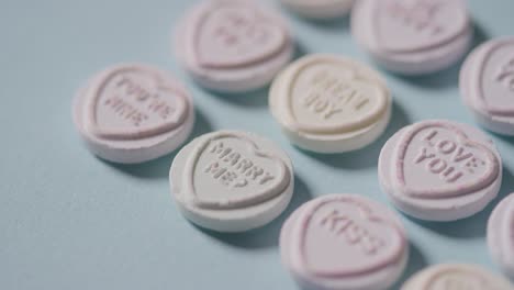 full frame shot of person sweeping away heart candy with romantic messages of love on blue background