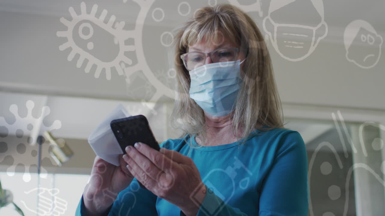animación de iconos de covid 19 sobre una mujer caucásica mayor que usa una máscara facial desinfectando un teléfono inteligente