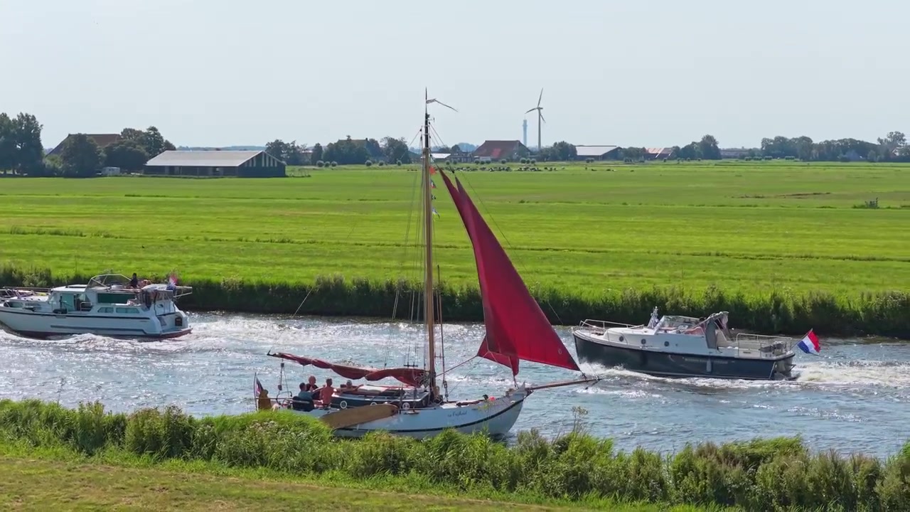 Seilbåt med røde seil navigerer en kanal på den nederlandske landsbygda
