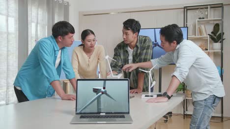 a laptop on the table is showing the video of wind turbine while asian engineers group discussing about work at the office