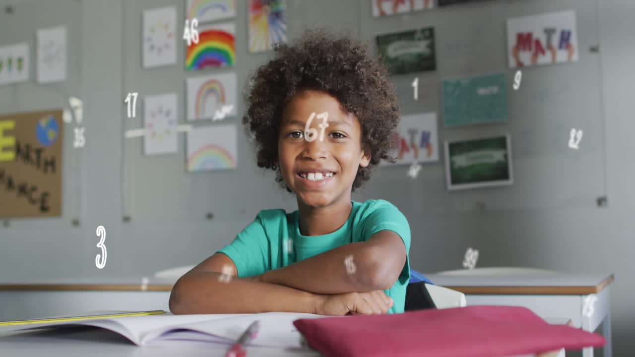 Animazione di numeri su un felice scolaro birazziale seduto al banco in classe e sorridente.