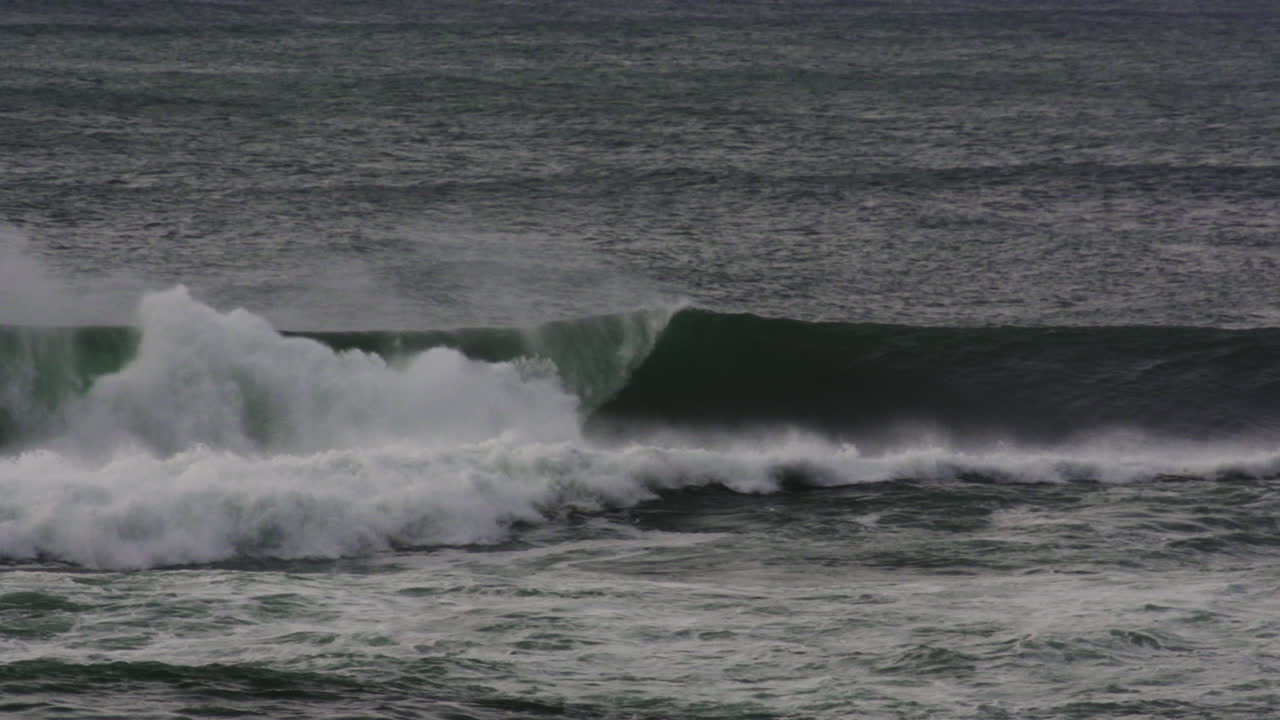 Ocean swell pushes to shore with heavy foam and rolling form under gray dusk sky