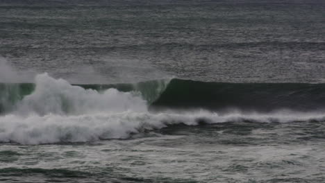 ocean swell pushes to shore with heavy foam and rolling form under gray dusk sky