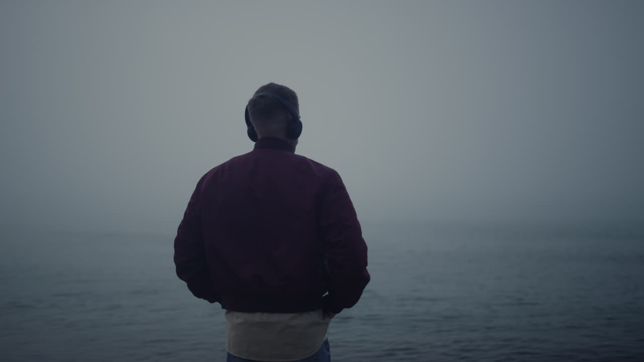 안개가 많은 해변에서 헤드폰을  ⁇ 고 춤을 추는 남자