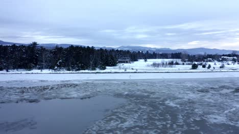 Drone-starting-from-the-frozen-water-level-and-moving-up-on-a-forest-and-village-on-a-winter-day