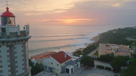 drone view  lighthouse standing on calm coast under orange sunset sky.