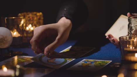 primer plano de una mujer dando una lectura de cartas del tarot en una mesa a la luz de las velas sosteniendo la carta del mundo 3