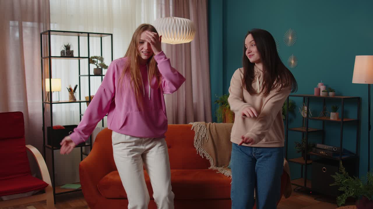 Happy two teenage girls siblings or bloggers couple dancing at home having fun enjoying trendy dance