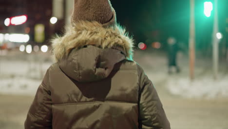 first-person view of a woman in a winter coat with a fur hood walking at night, while blurry people move in the background