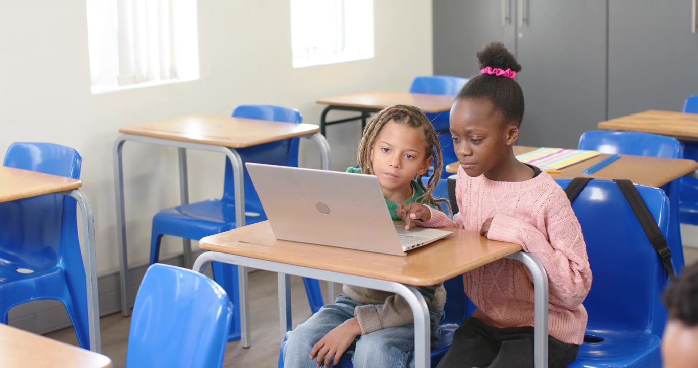 Studenti di diverse etnie che guardano il contenuto del laptop, collaborando alla scrivania, ragazza che usa il trackpad, ragazzo che osserva.