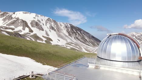 wide angle drone shot flying towards an observatory located on top of a mountain with an incredible mountains landscape in the distance in the region of abruzzo in italy during the winter