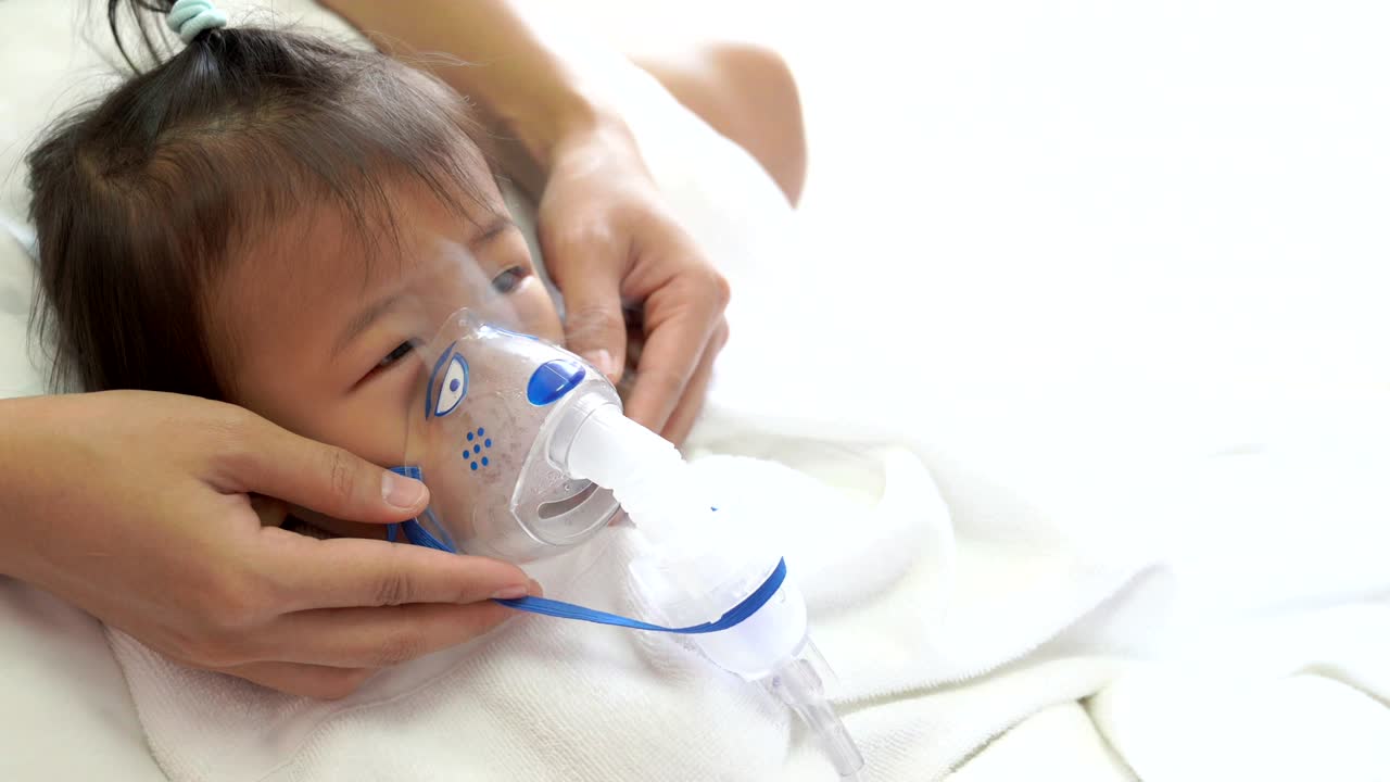 Bambina asiatica in terapia respiratoria accudita dalla madre.
