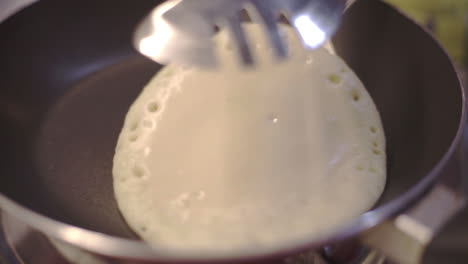 foamy pancake being flipped in a frying pan closeup