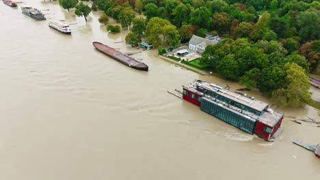 aerial footage of the danube river overflowing its banks in bratislava, submerging the riverbank and surrounding trees. boats and floating structures are caught in rising floodwaters.