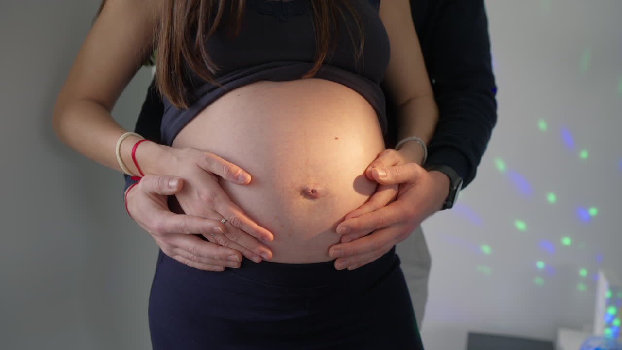 Manos de pareja acunando el vientre de mujer embarazada