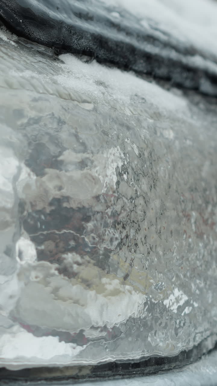 Close-up of a car's frosted taillight covered with ice and snow, highlighting intricate ice patterns and winter's chilling effect on vehicle surfaces