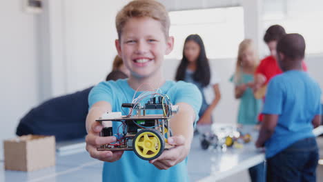 Retrato-De-Un-Estudiante-Varón-Sosteniendo-Un-Vehículo-Robot-En-Una-Clase-De-Codificación-Informática-Después-De-La-Escuela